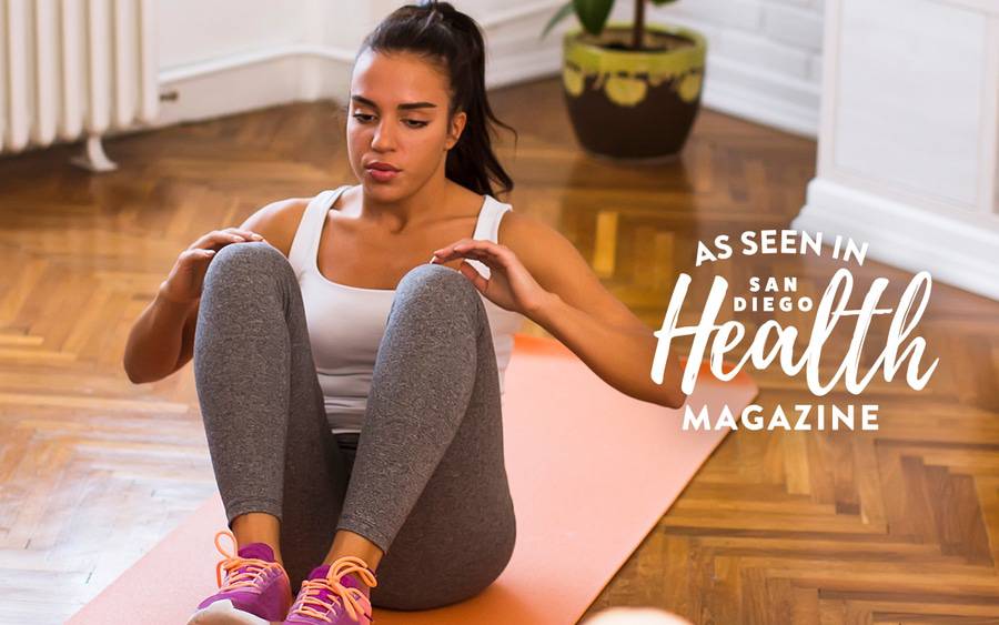 A woman working out at home while on a yoga mat, demonstrating how to get back on track with your fitness goals. 