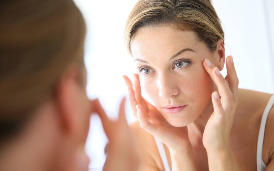 A woman checks her eyes in the mirror.