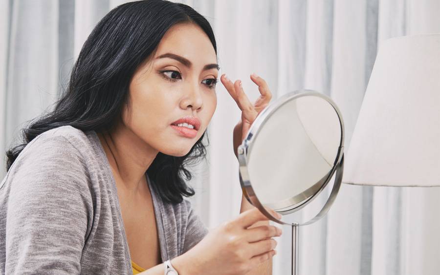 A woman checks the mirror after a thread lift cosmetic procedure.