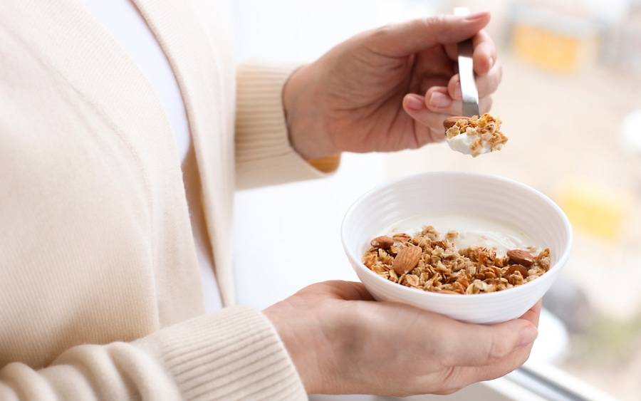 Older woman scoops healthy yogurt with spoon.