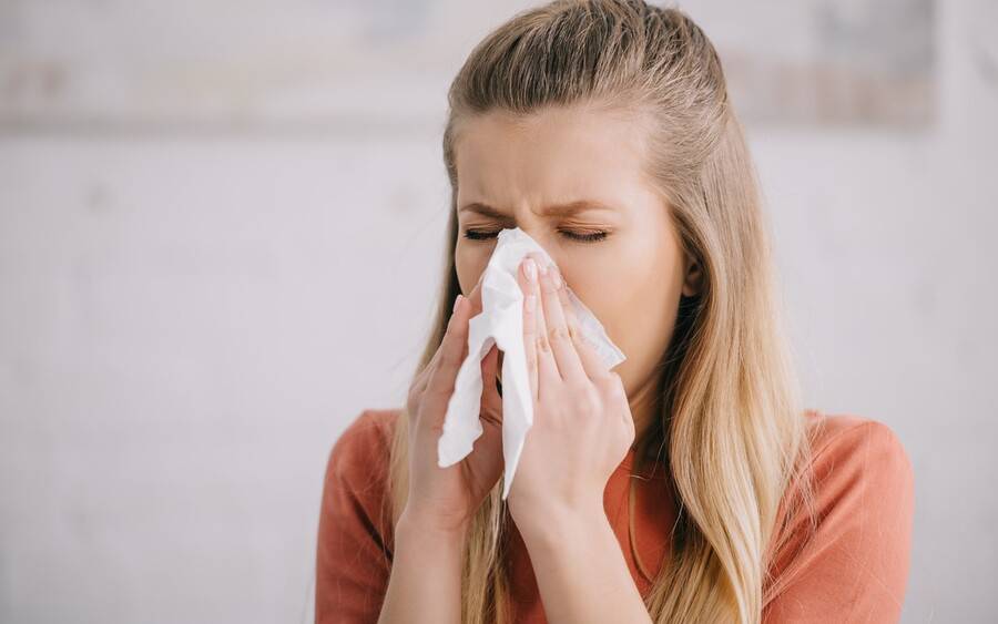 Woman with allergy triggered asthma sneezes into tissue.