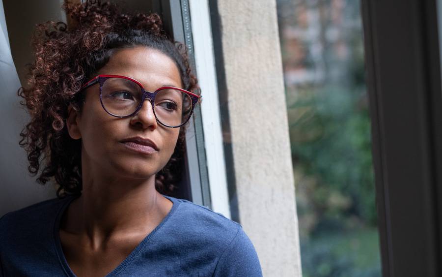 An African-American woman with depression and heart disease looks out the window.