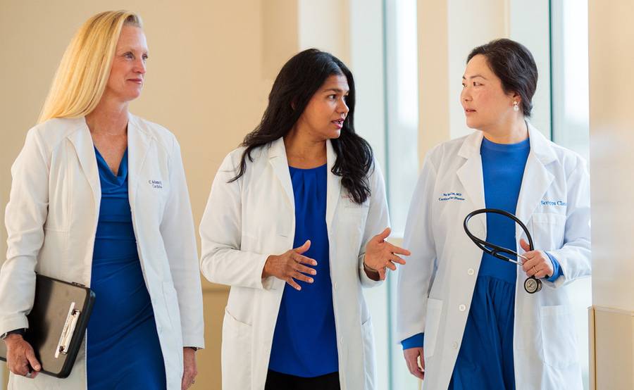 Three female cardiologists walking and discussing women's heart care issues and topics.