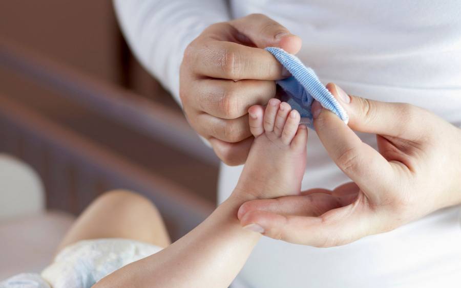 A young dad puts a sock onto a newborn baby's foot.