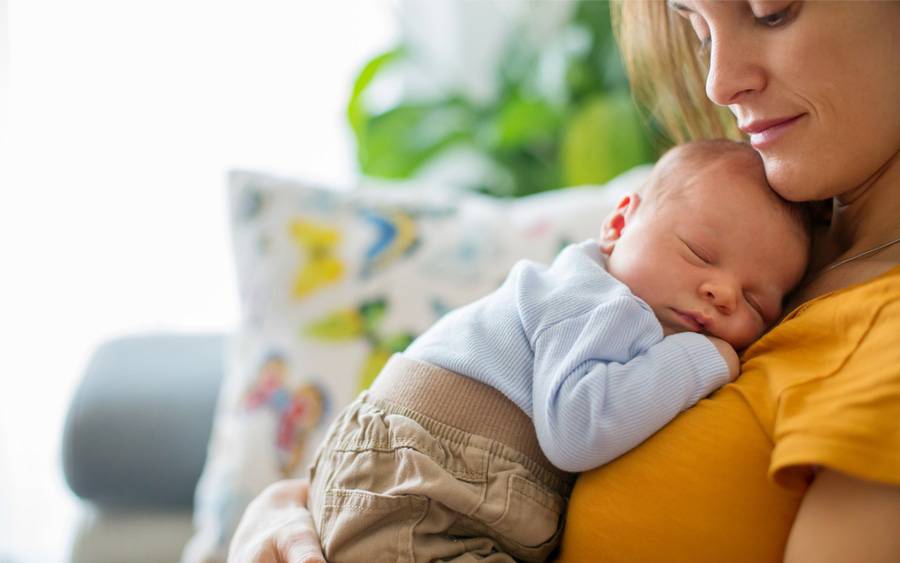 A young mother tenderly holds her newborn on her chest.