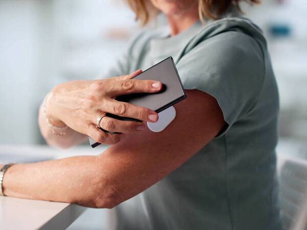 A woman checks her glucose number by scanning her mobile device to a patch on her arm.