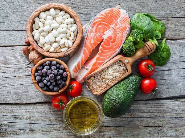 Heart healthy foods displayed in a heart shape including blueberries, tomatoes, oats, avocado, salmon, broccoli, spinach and olive oil.