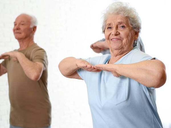 Three older adults, both men and women, participate in a group exercise to help with balance.