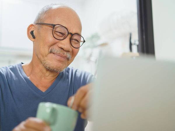 An older man wearing earbuds and looking at a laptop