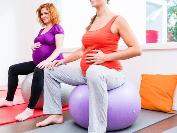 Two pregnant women sitting on exercise balls during a prenatal class
