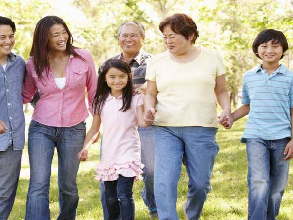 A multigenerational Asian family smiles as they take a walk together outdoors.