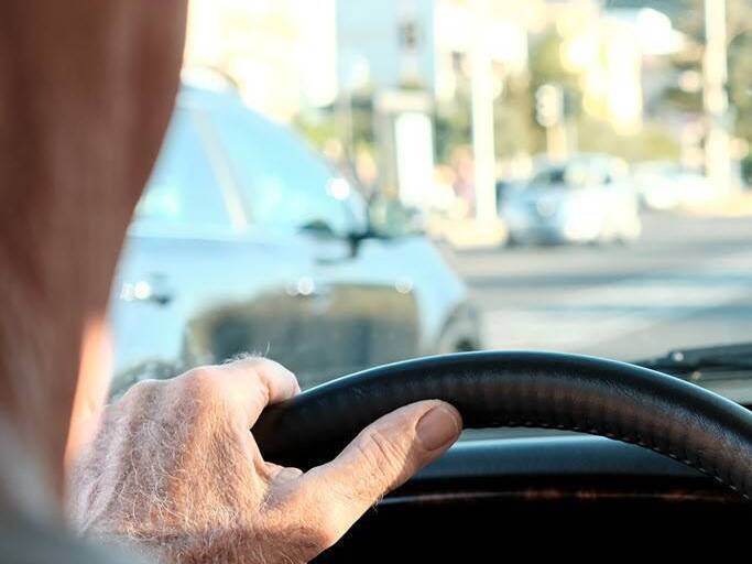 An older person drives a car on a city street.