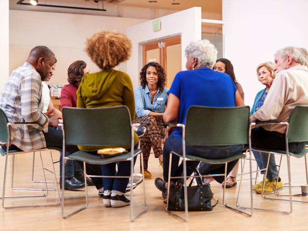 A diverse group of people sits in a circle discussing alcohol-related disease led by a medical expert.