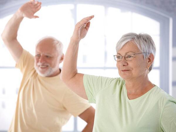 A senior man and woman stretch their arm up in an exercise class designed to improve circulation and mobility.