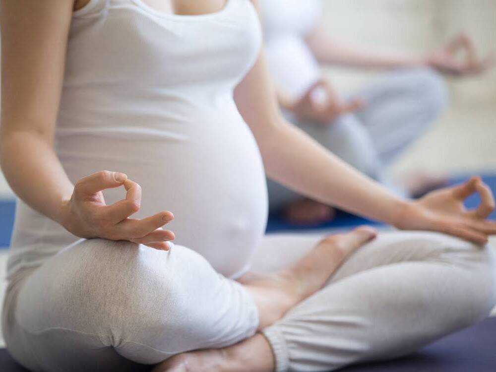 A young pregnant woman sits on the floor while participating in a prenatal yoga class.