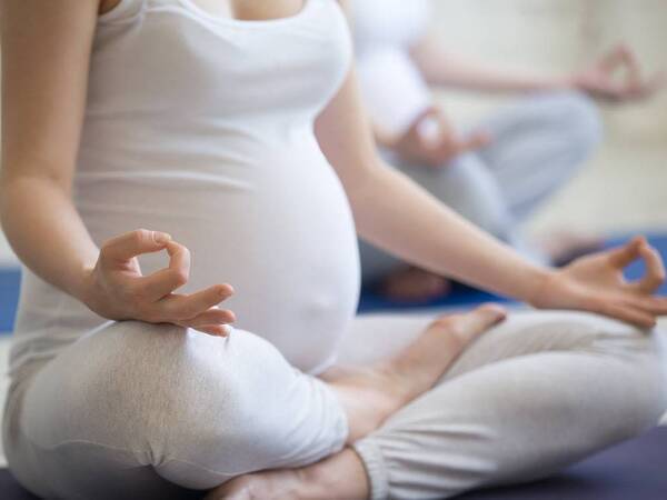 A young pregnant woman sits on the floor while participating in a prenatal yoga class.