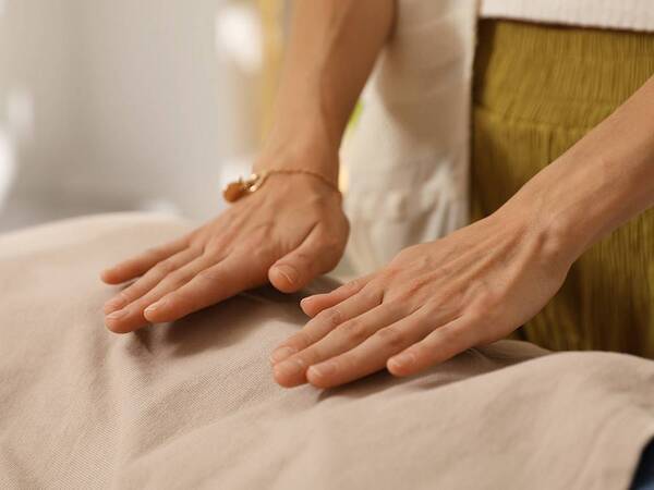 A practitioner places their hands on a patient's back in a healing touch session.