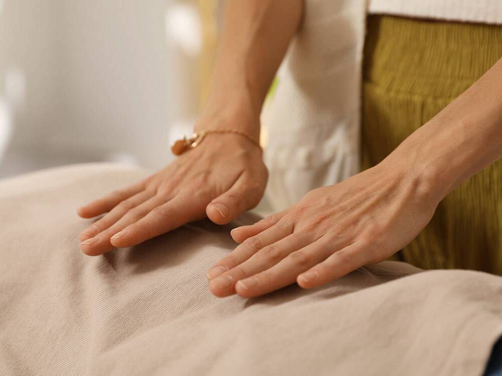 A practitioner places their hands on a patient's back in a healing touch session.