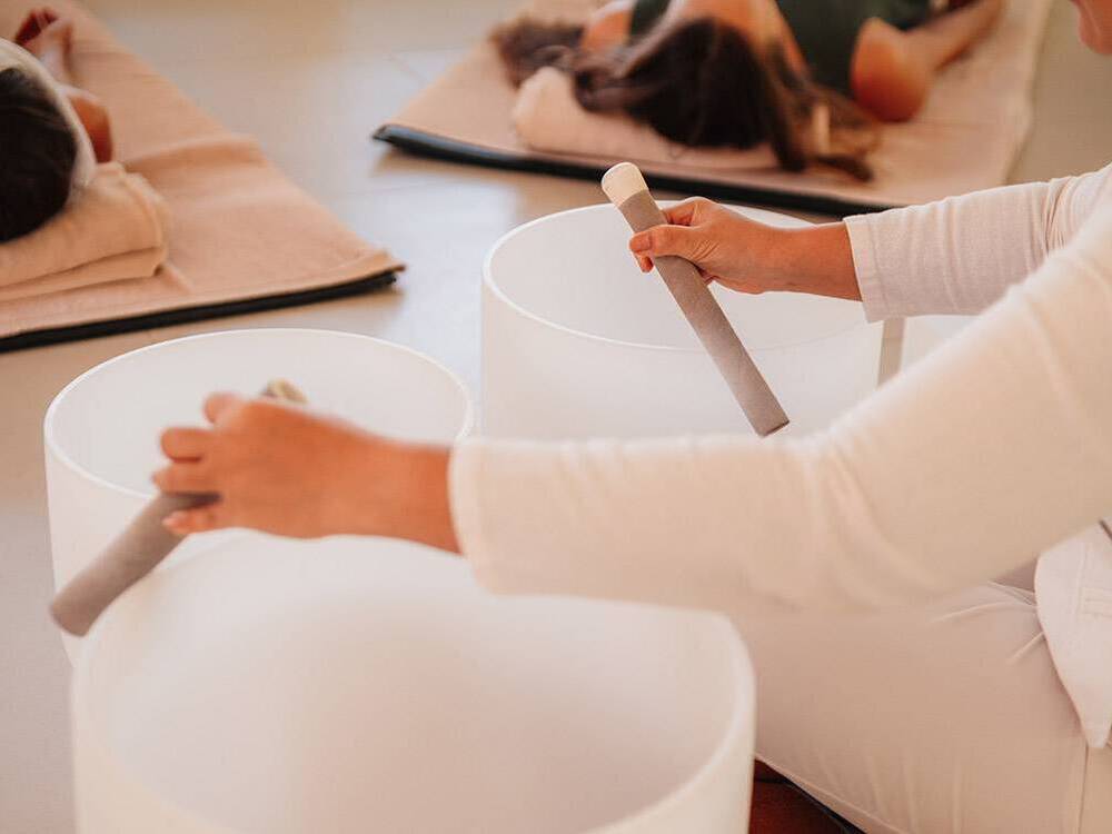 Cancer patients relax in savasana pose with mediative sound produced by a person tapping batons on large bowl-like instruments.