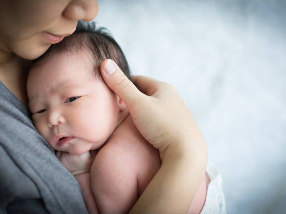 A woman nurtures a newborn in a diaper, holding them closely against her chest.