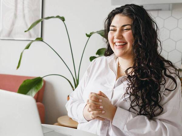 A young woman smiles as she looks at her laptop while participating in an online webinar on weight management.