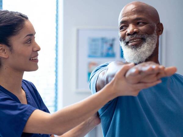 A physical therapist supports a patient's arm as he stretches his arm forward to help with joint stiffness from cancer treatment.