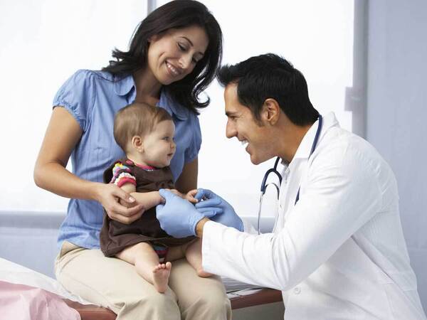 A friendly Scripps Health doctor engages with a small child and her mother in a clinical setting.