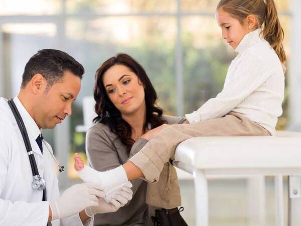 A primary care doctor checks the foot of a little girl who injured herself while playing. She sought immediate help at an urgent care clinic.