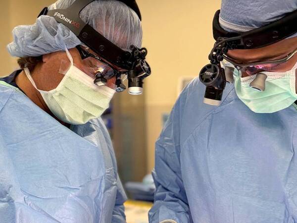 Two surgeons dressed in scrubs perform a procedure to remove a tumor.