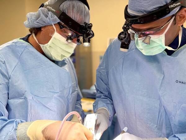 Two surgeons dressed in scrubs perform a procedure to remove a tumor. 