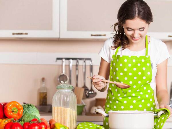 A woman prepares fresh produce and healthy grains in a kitchen, focusing on recipes designed for cancer patients. 