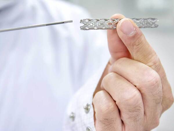 A doctor wearing a lab coat holds a heart stent