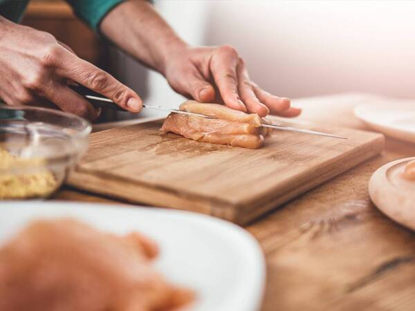 A person cooking chops chicken on a separate board to prevent foodborne illness.