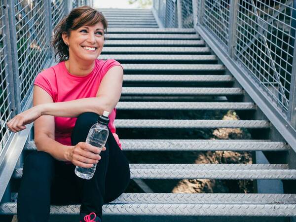 A woman in her 50s rests with a water bottle on her hand after a workout.