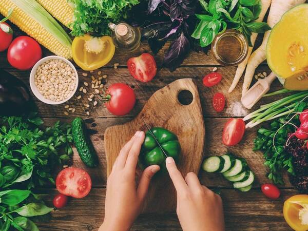 A woman cuts a bell pepper on a table surrounded by other organic foods.