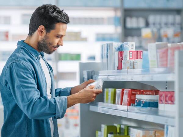 A young man reads the label of a over the counter pain medicine at a pharmacy.