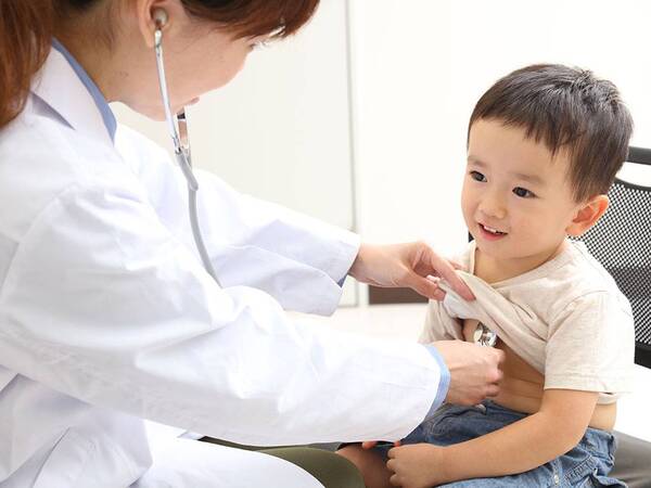 A young child sits in a doctor's office while a pediatrician uses a stethoscope.