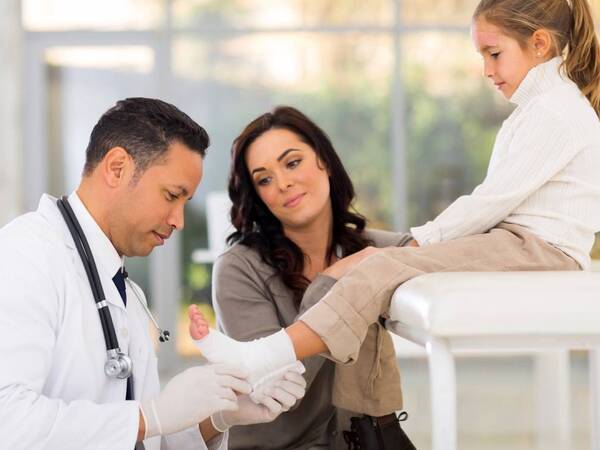 A primary care doctor checks the foot of a little girl who injured herself while playing. She sought immediate help at an urgent care clinic.