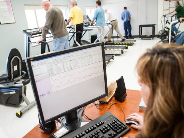 A clinical provider monitors a heart rate machine while heart patients undergo cardiac rehabilitation exercises.