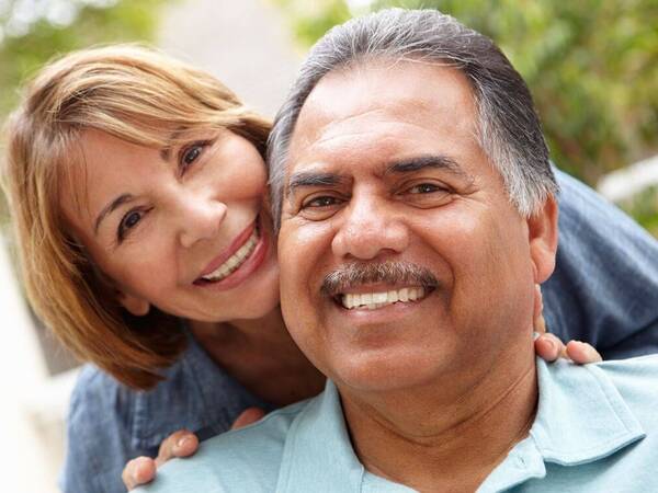 A husband and wife in their 50s and 60s pose for a photo while enjoying a day at the park.