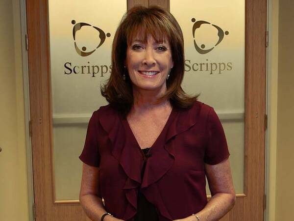 A smiling Susan Taylor portrait standing before two doors embossed with Scripps logo. 