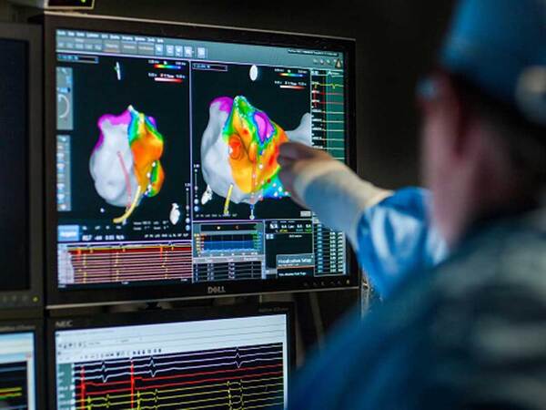 A physician in scrubs points to a digital screen showing a heart image in a darkened room. 