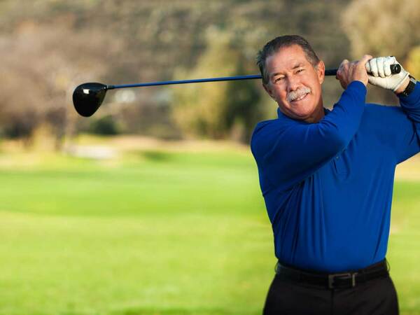 A smiling Gary Collins swings a golf club after a successful hip replacement at Scripps Health. 