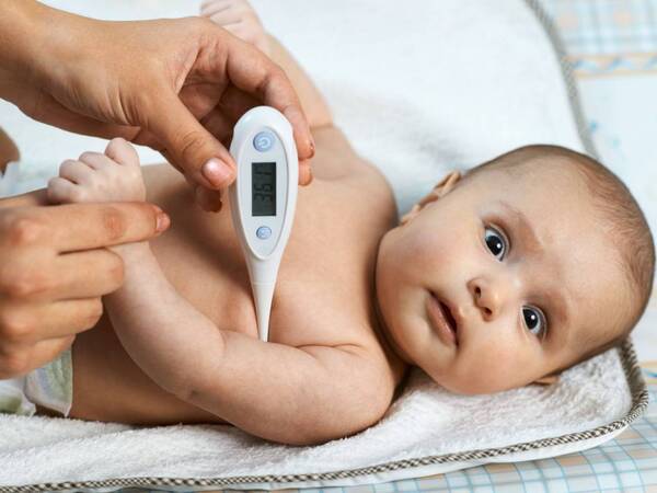 A baby lays down before getting temperature taken with a fever thermometer.