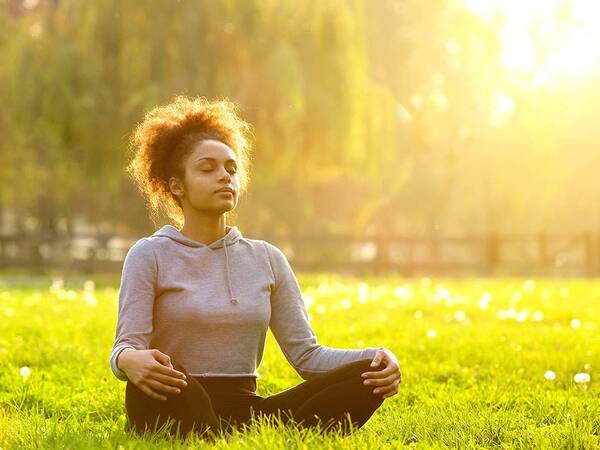 A woman meditates in a grassy field on a sunny day.