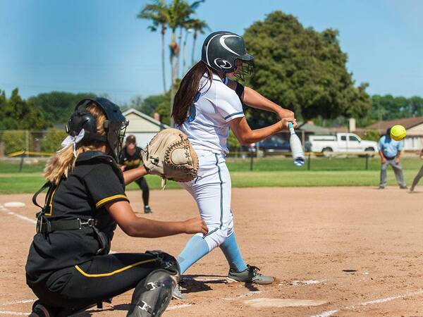 A batter swings at a pitch during a softball game on a sunny day.