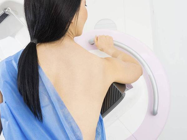 A woman stands in front of a mammography machine.