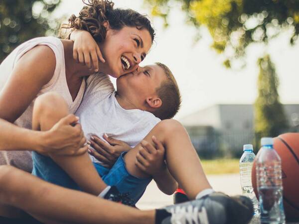 A mother hugs her son who returns the affection with a kiss. A basketball by their side suggests he is staying active during school spring break.