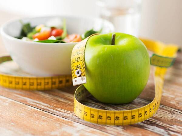 A measurement tape wraps around a green apple and salad bowl, representing weight loss truths and myths.