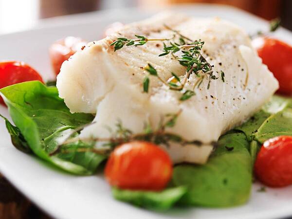 A plate of white fish with rosemary and cherry tomatoes on a bed of baby spinach represents a healthy diet that may help prevent cancer.
